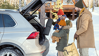 Family of three in warm winter clothing loading luggage into the back of a vehicle in snowy weather