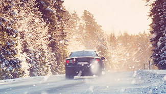 A black car driving on a snowy, icy road through a remote, wooded area.