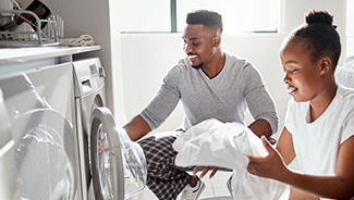 A young couple works together to put laundry into their front-loading washing machine.