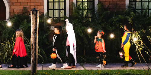 Five children in Halloween costumes trick-or-treating in the evening.