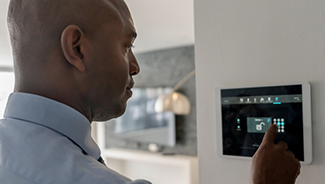 A man in a blue shirt ensures the doors in his  house are locked using a home security system.