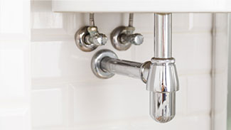 Close up view of pipes and water supply valves underneath a bathroom sink.