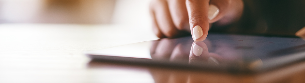 Closeup of a person with white painted nails pointing at a tablet PC on a wooden table.