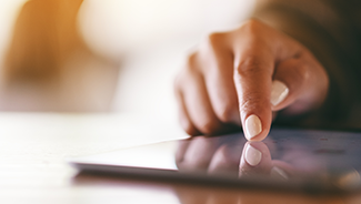 Closeup of a person with white painted nails pointing at a tablet PC on a wooden table.