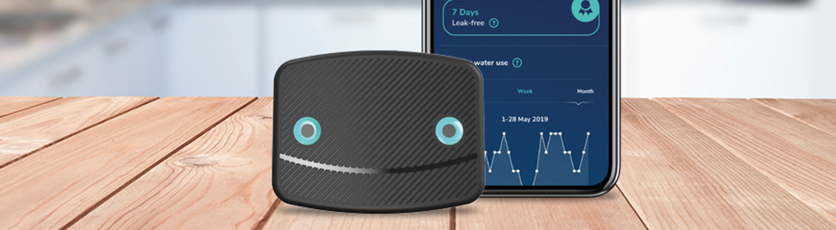 A LeakBot water leak detection device sits on a table next to a smart phone displaying the LeakBot app.