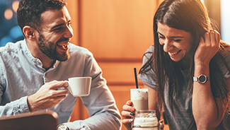 A man, wearing a white denim shirt, and a woman, wearing a gray T-shirt, are drinking coffee together at a cafe.