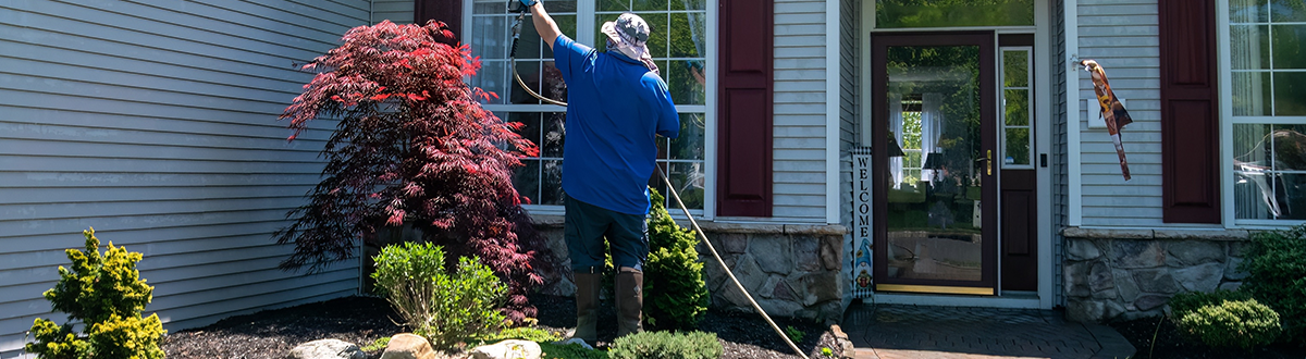 A man with a water hose power washing the roof and siding of a house