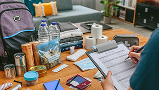 Close up of home emergency supplies near a person marking items off an emergency planning checklist